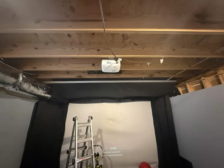 A golf-sim bay mid-install: a ladder against the screen, projector overhead, ready for the light bar to go in.