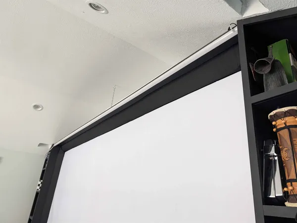 A slim 45-degree aluminum diffuser channel mounted along the top edge of a golf-sim impact screen.