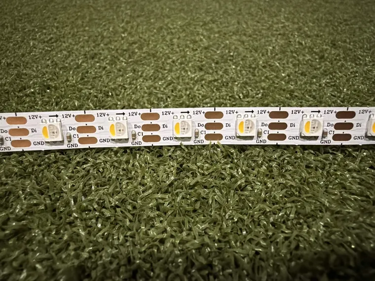 Close-up of the addressable LED strip showing the 12V+, data and ground pads and the marked cut lines between LEDs.