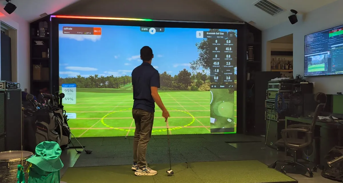 A wide view of an indoor golf-sim bay with the SimLight Golf LED strip running above the screen.